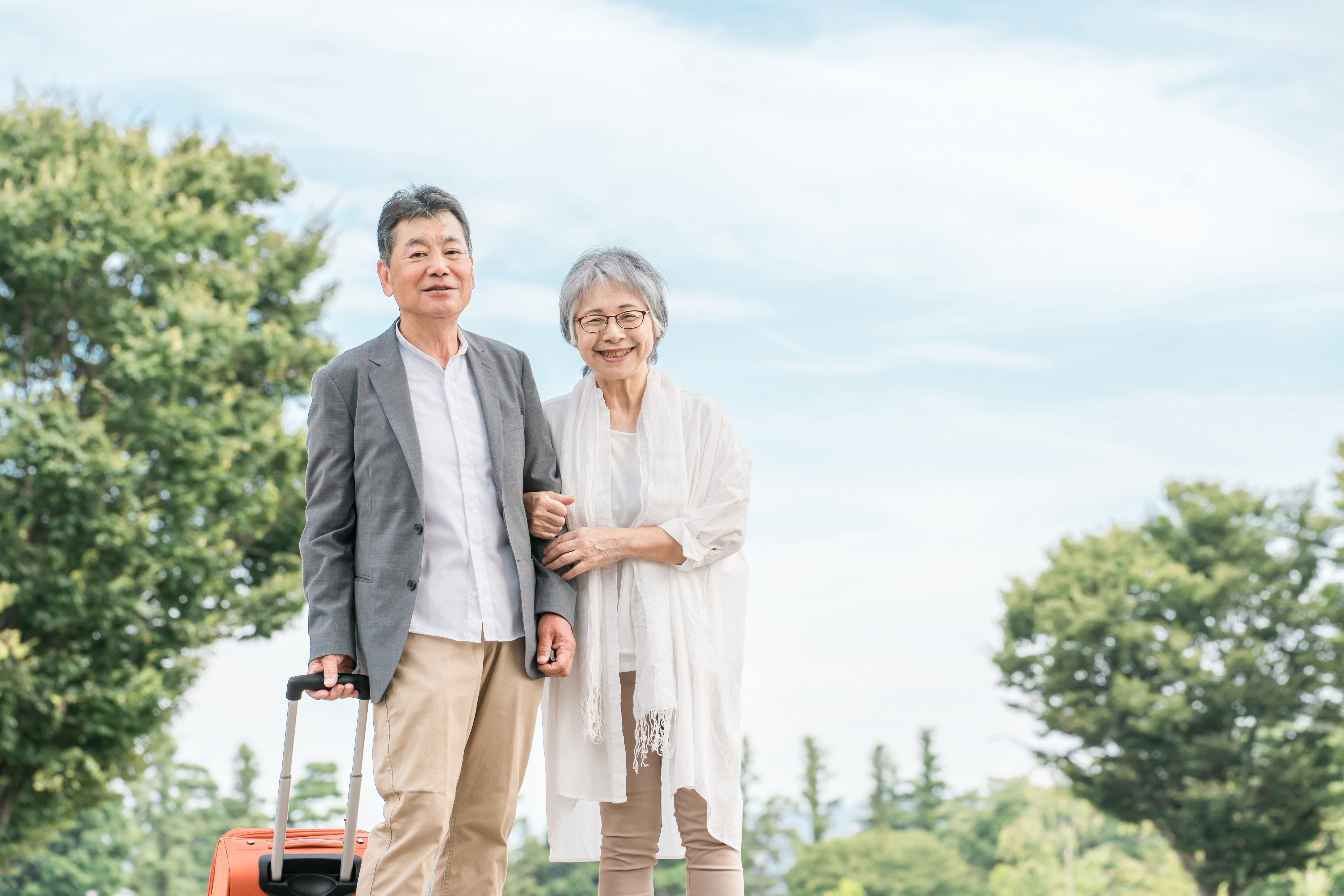 スーツケースを持って旅行に出かける笑顔のシニア夫婦