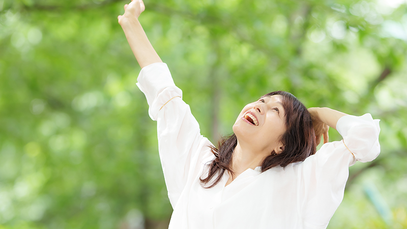 朝日を浴びながら笑顔で背伸びをするシニア女性