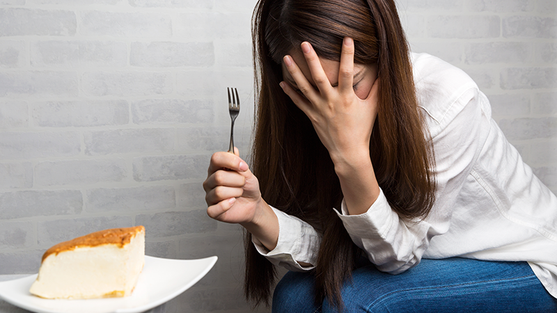チョコレートケーキを前にして食べるか悩む女性