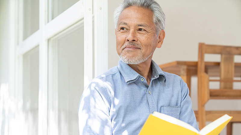 明るい窓際で笑顔で前を向いて微笑む、元気な日本人高齢男性のイメージ