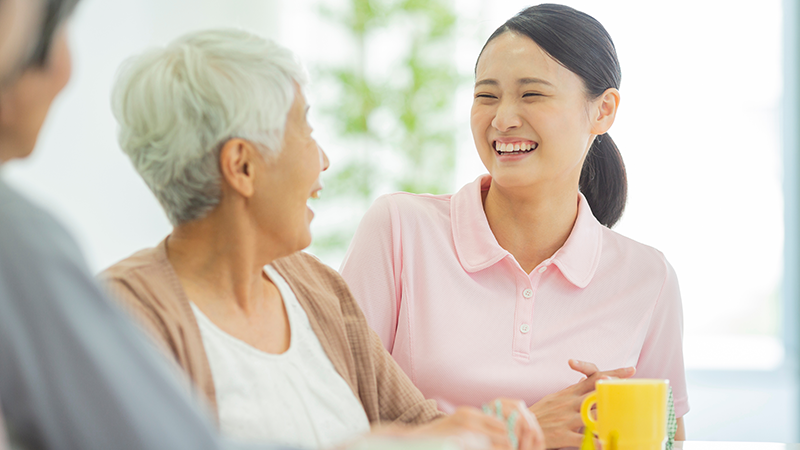 自宅や介護施設で家族（または介護スタッフ）と笑顔で会話するシニアのイメージ